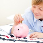 Cute boy putting a coin in a piggybank at home